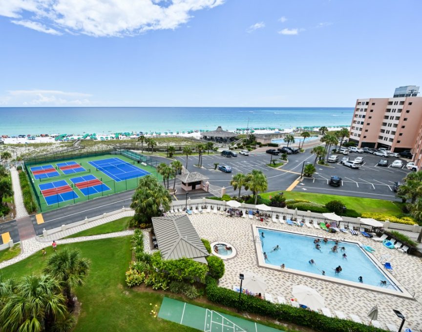 Resort pool, hot tub and tennis and pickleball courts, seen from above, with the Gulf behind